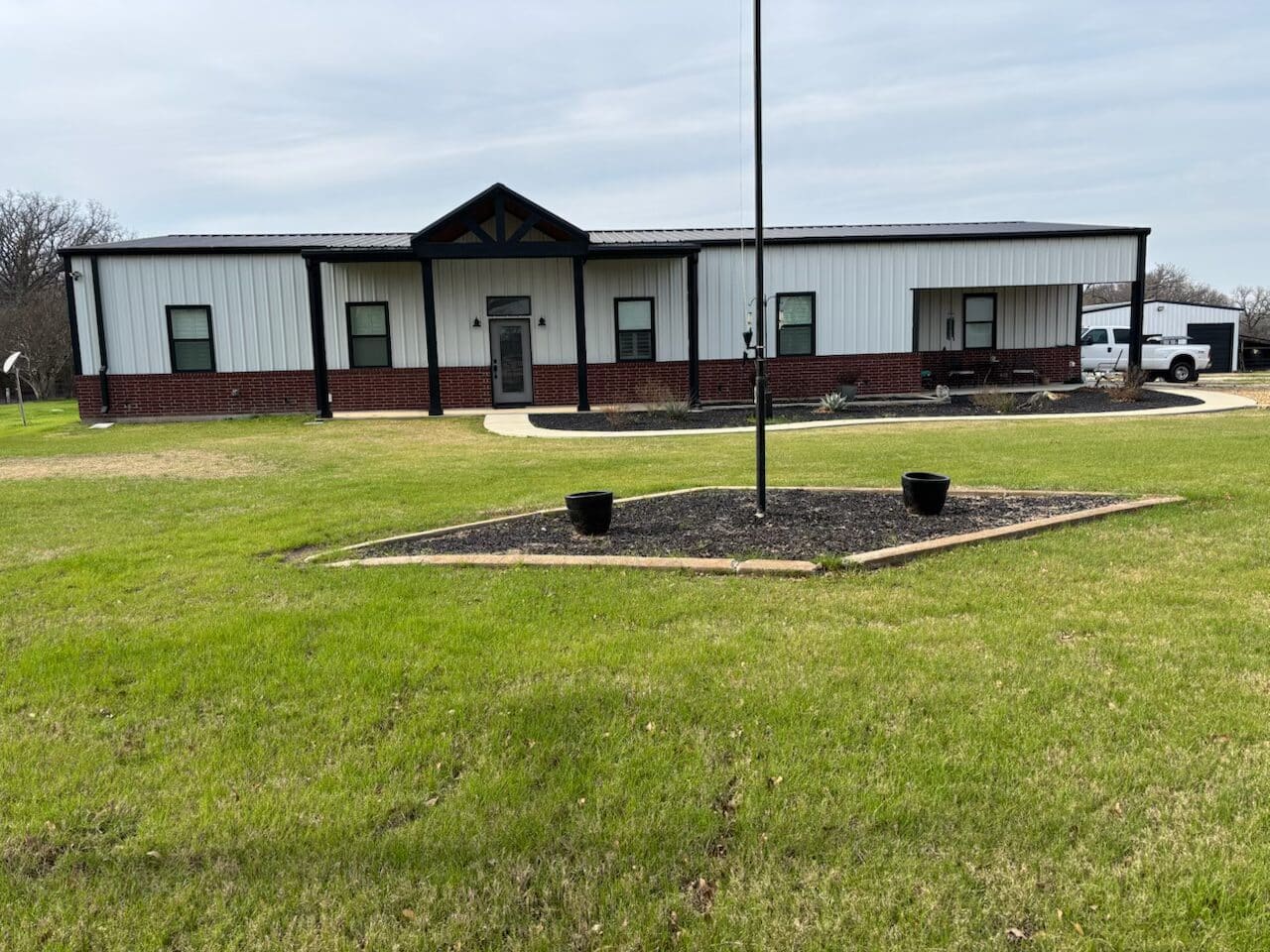 Completed custom barndominium in Central Texas with metal siding, brick exterior, and covered front entry on landscaped rural property.