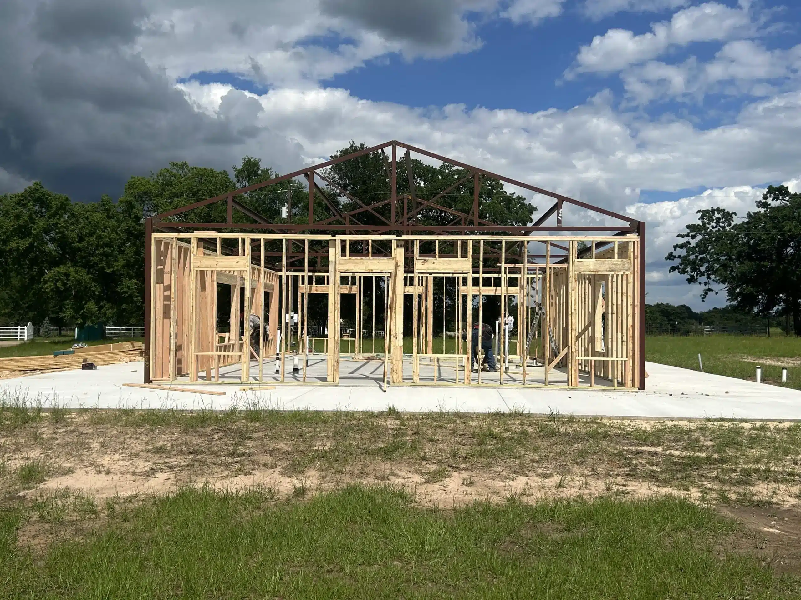 Barndominium framing on a concrete slab during construction, with trees around the site