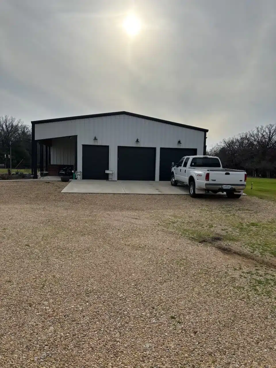 Black metal barndominium with garage doors and a gravel drive on rural East Texas land